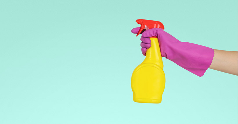 Hand wearing cleaning glove holding spray bottle.